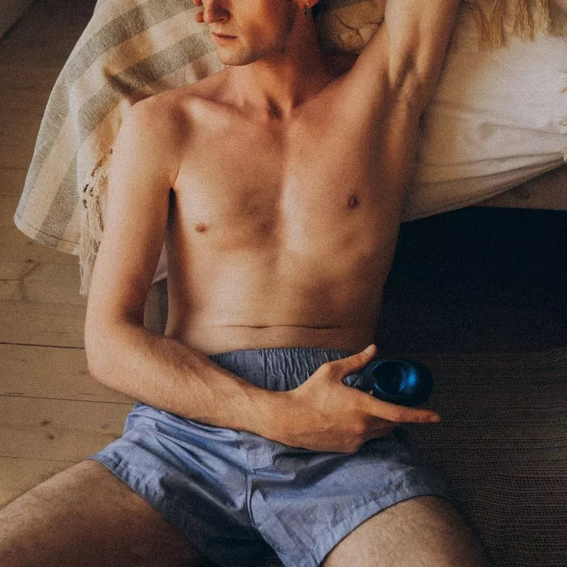 Man sitting on the floor holding Manwan Sub One Tapping Male Stimulator by Lovely Planet while wearing light blue boxer shorts.