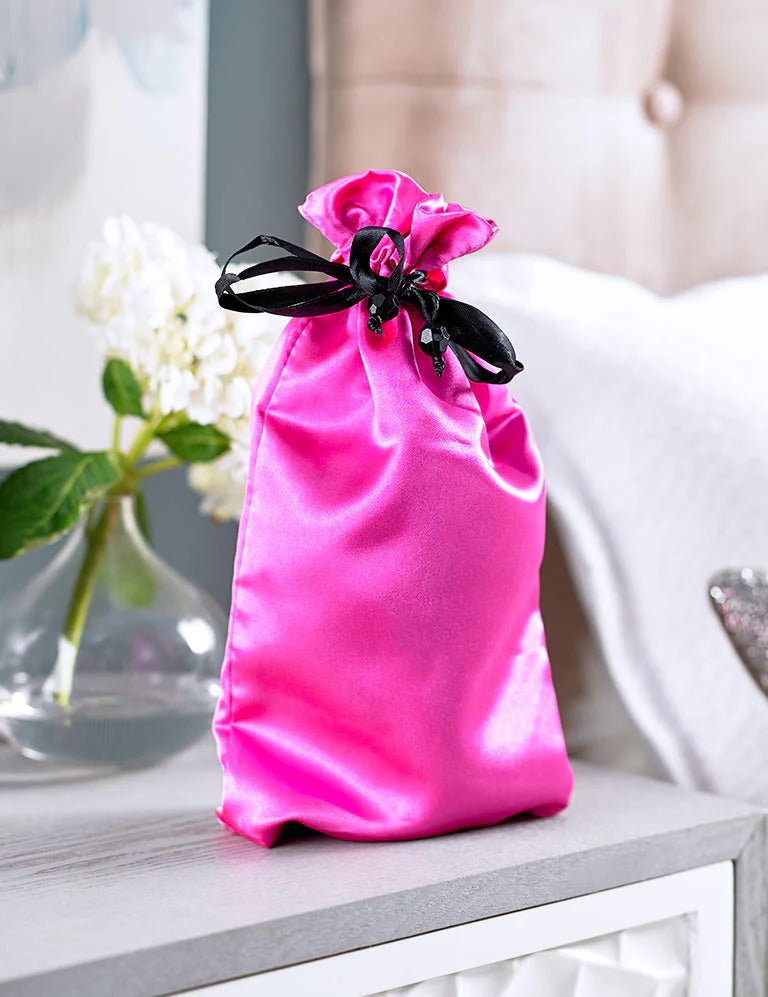 Pure Romance's Hot Pink satin drawstring toy tote bag with black closure on nightstand by bed. Made by Sugar Sak.