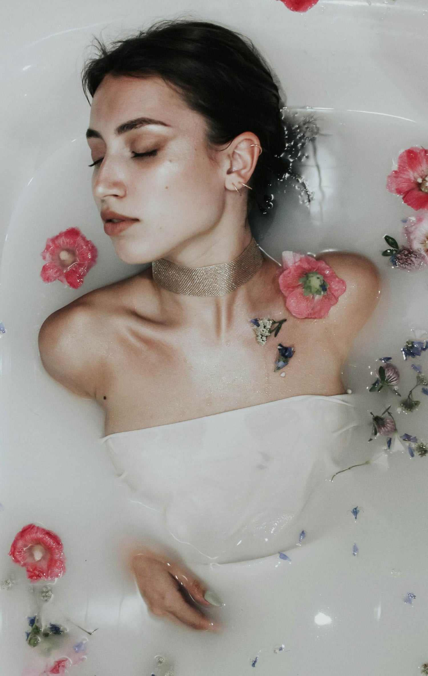 Woman in milk bath surrounded by flowers, relaxed with eyes closed