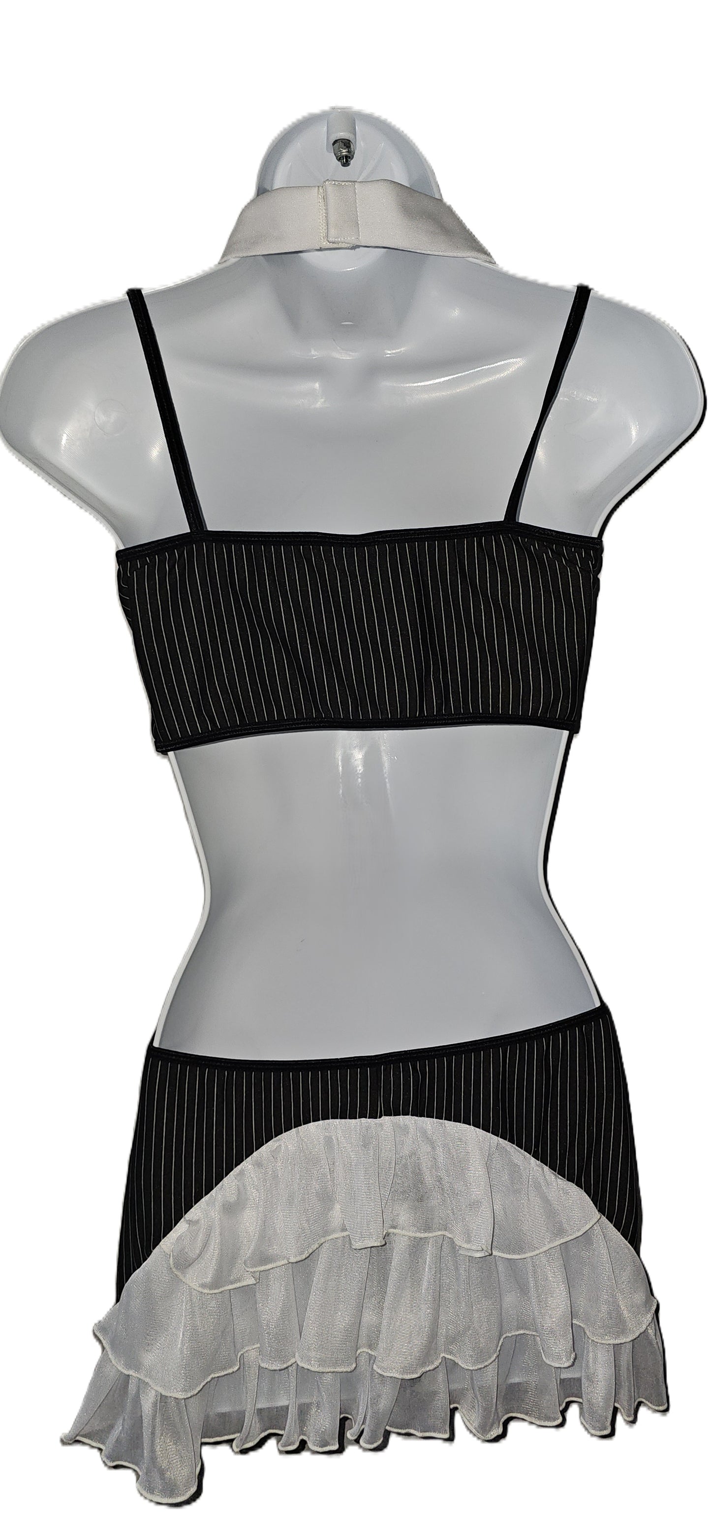 A black and white ruffled two-piece outfit displayed on a white mannequin torso. The top is a black ribbed bandeau-style crop top with thin straps, and the skirt is black with a wide white ruffled overlay at the hem. Dreamgirl 4-piece pinstripe lingerie set with chiffon camisole, attached necktie, and decorative buttons