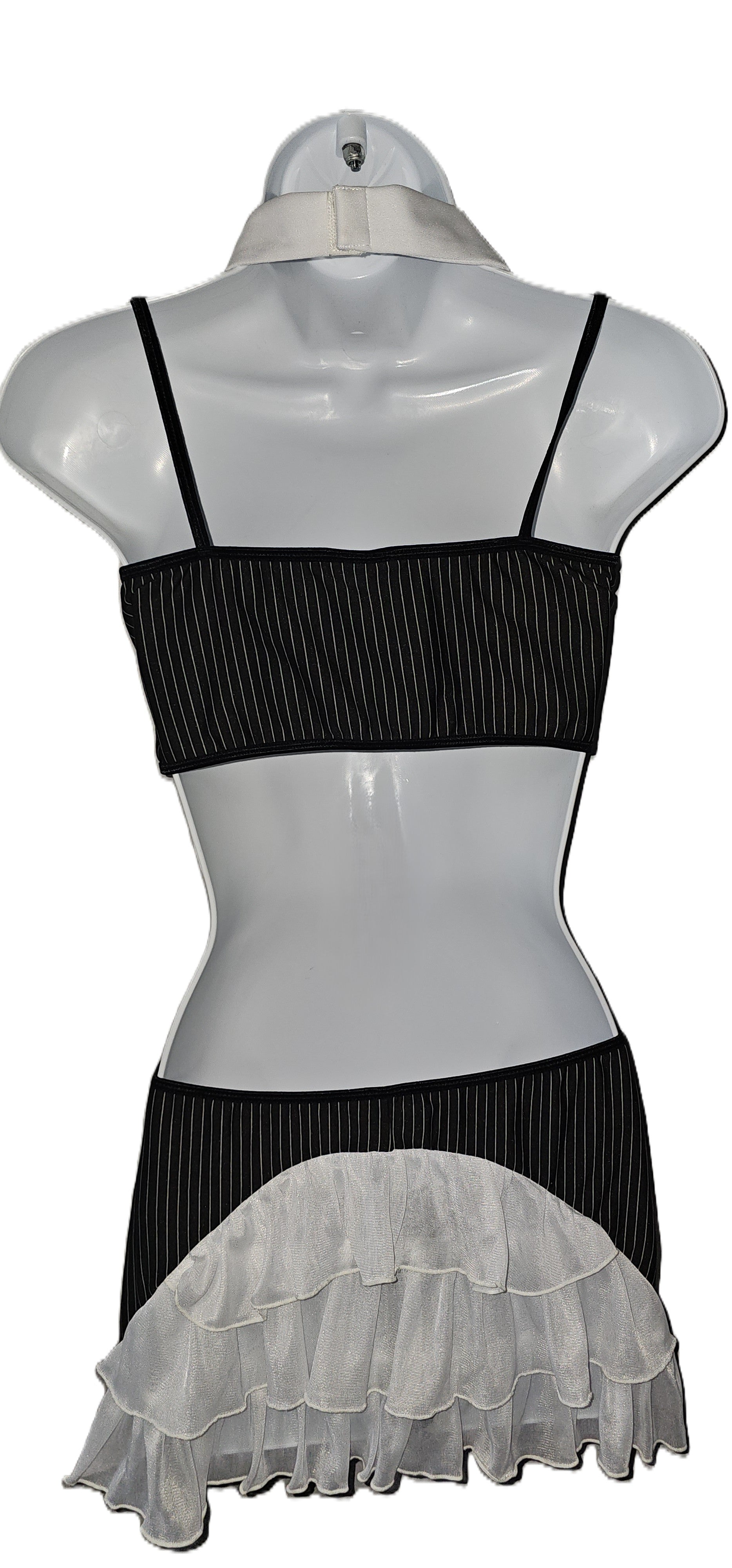 A black and white ruffled two-piece outfit displayed on a white mannequin torso. The top is a black ribbed bandeau-style crop top with thin straps, and the skirt is black with a wide white ruffled overlay at the hem. Dreamgirl 4-piece pinstripe lingerie set with chiffon camisole, attached necktie, and decorative buttons