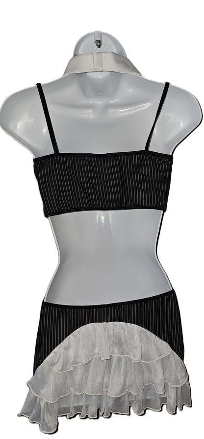 A black and white ruffled two-piece outfit displayed on a white mannequin torso. The top is a black ribbed bandeau-style crop top with thin straps, and the skirt is black with a wide white ruffled overlay at the hem. Dreamgirl 4-piece pinstripe lingerie set with chiffon camisole, attached necktie, and decorative buttons
