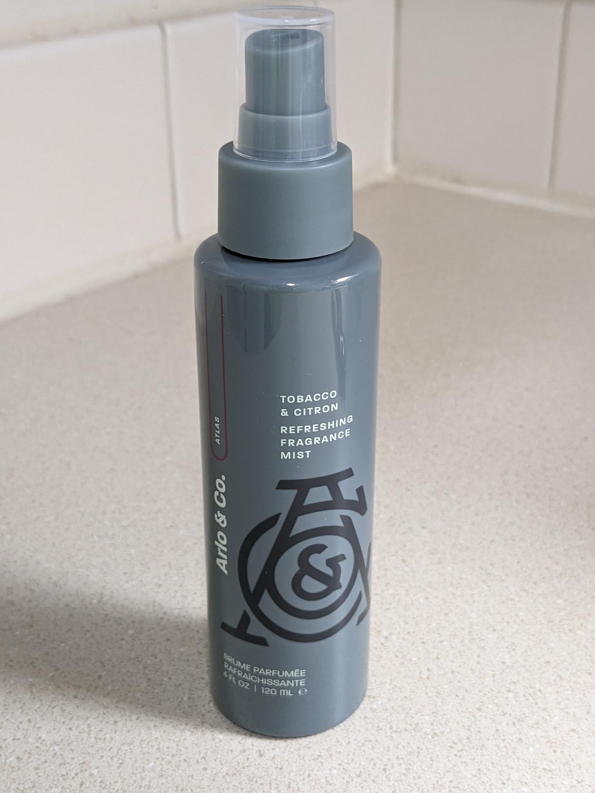 A bottle of Pure Romance Arlo & Co Refreshing Fragrance Mist in Tobacco & Citron scent, standing on a light countertop against a tiled backsplash.