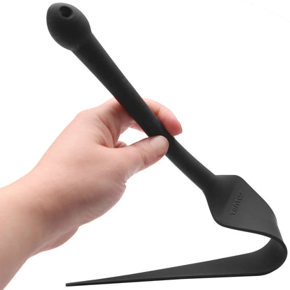A hand holding a Tantus black silicone Dragon Tail Love Whip with a long handle featuring product flexibility, shown against a plain white background.