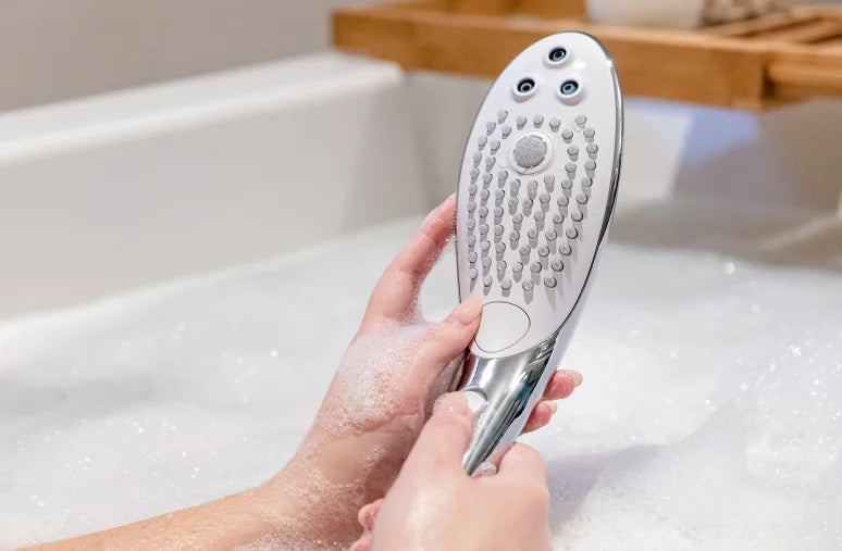Hand holding a Chrome Womanizer Wave masturbation shower head over a bathtub filled with water