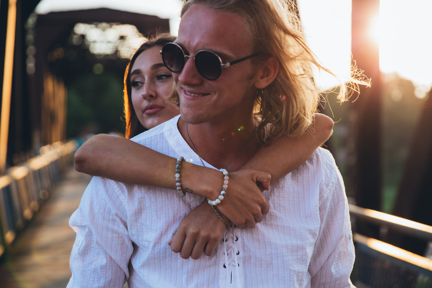 Couple embracing on a bridge with warm, sunlit background in a romantic moment, adult lifestyle, intimate outdoors, love and connection scene.