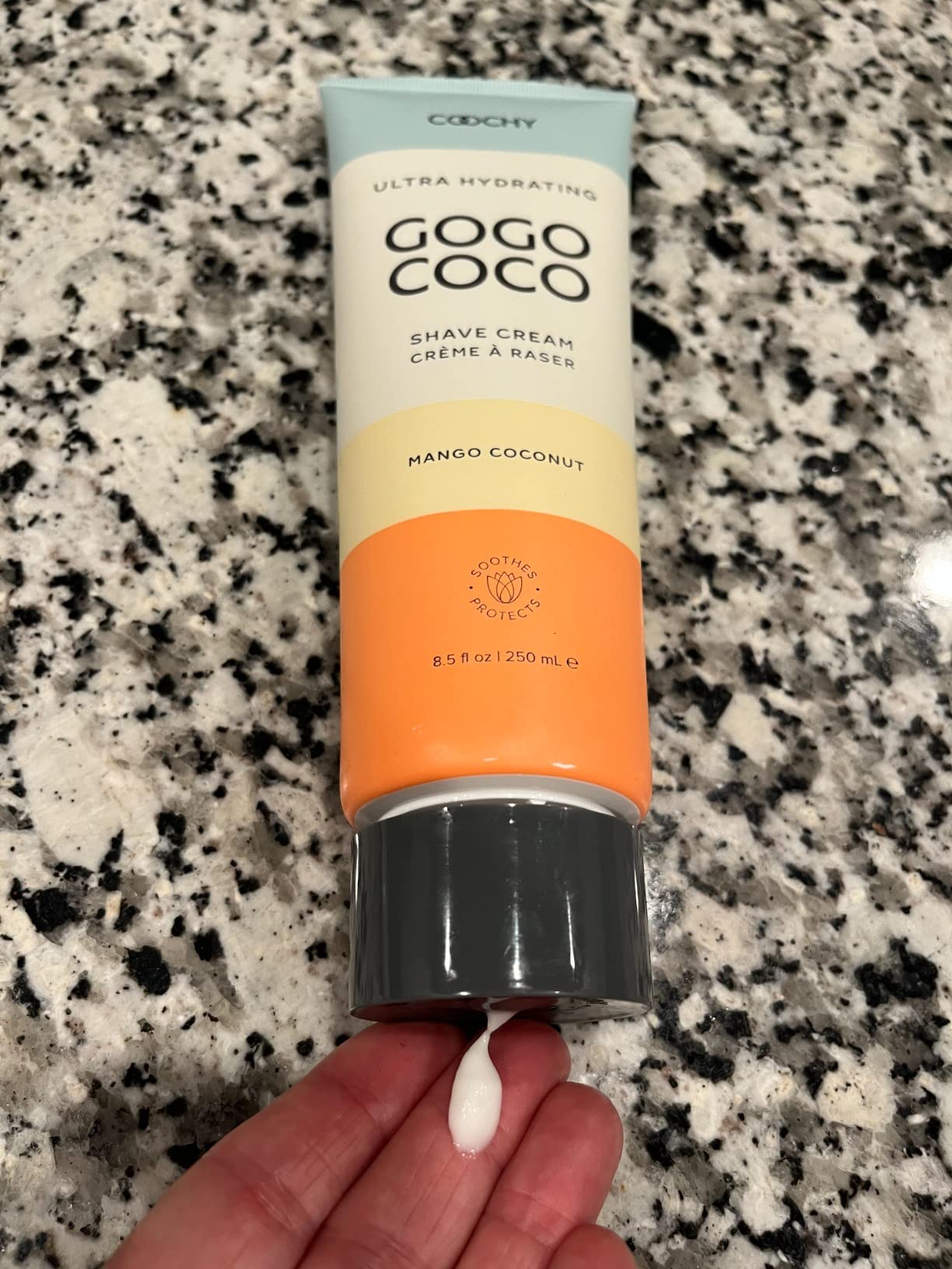 Gogo Coco shave cream twist to open tube dispensing shave cream onto a hand on a speckled countertop