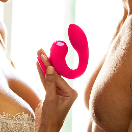 Woman with her partner holding a pink g-spot toy called Dual Gripp by JimmyJane against a blurred background