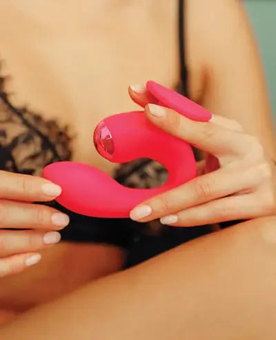 Person holding a Dual Gripp G-spot and couples toy by JimmyJane with a blurred background of her wearing black lingerie