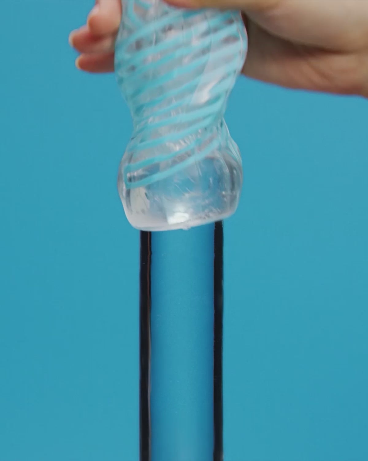Tenga Spinner DX male stroker in action with woman's hand sliding it on glass pole on a blue background.