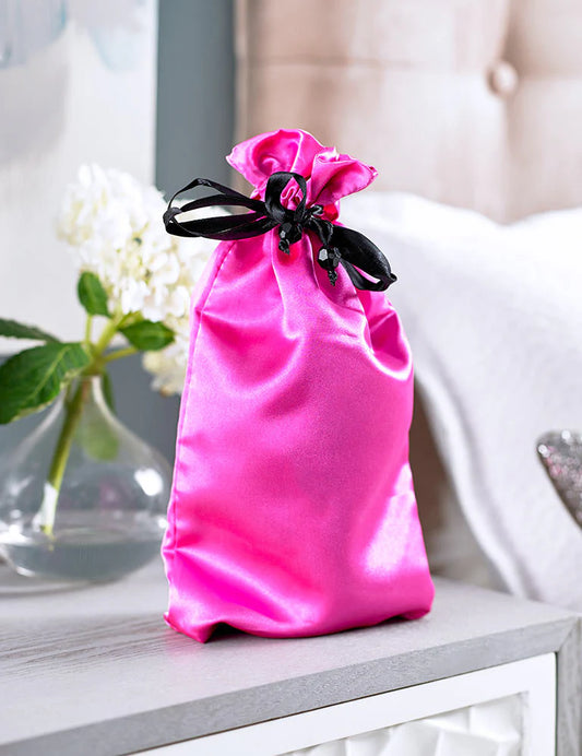 Pure Romance's Hot Pink satin drawstring toy tote bag with black closure on nightstand by bed. Made by Sugar Sak.