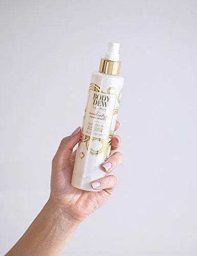 Hand holding a bottle of Body Dew Love Story by Pure Romance against a light gray background