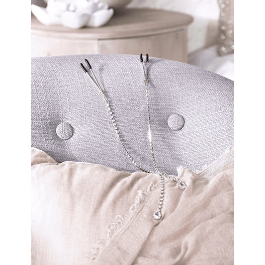 Silver and rhinestone nipple clamps by Pure Romance draped across a chair to show texture and elegance 