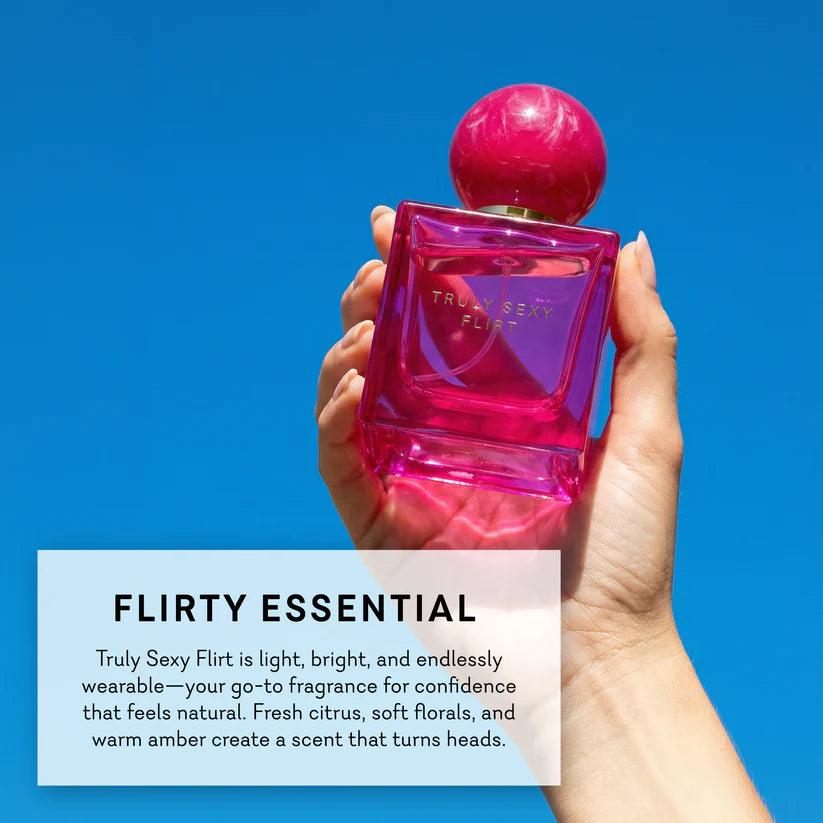 Hand holding a Pure Romance Truly Sexy Flirt pink perfume bottle with a blue background and product description text.
