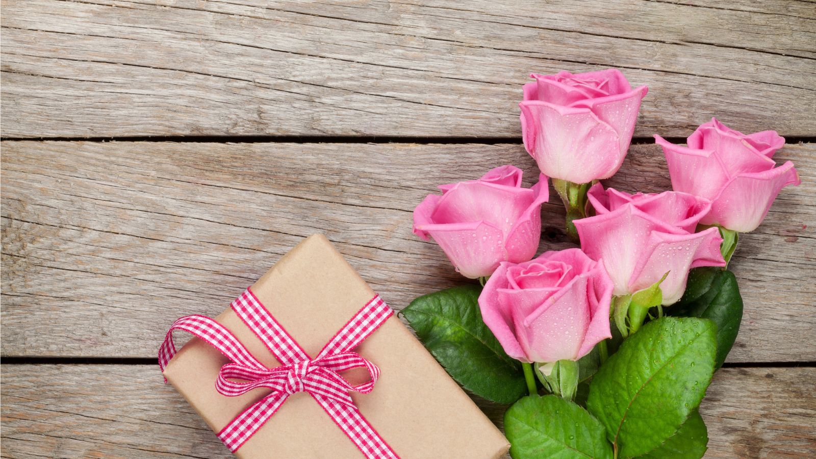 Gift box with pink ribbon and pink roses on a wooden surface
