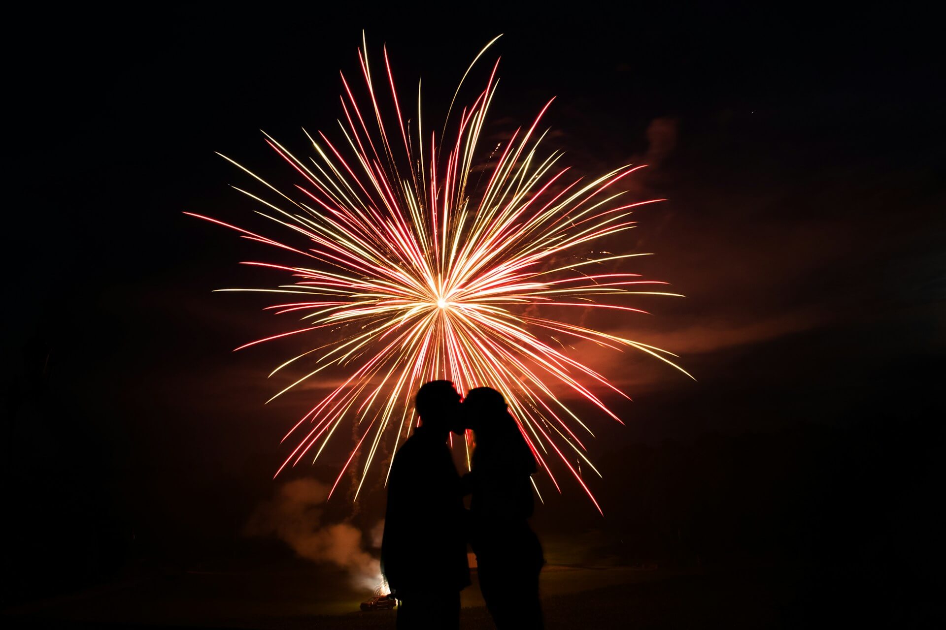 Two people silhouetted against a vibrant fireworks display in the night sky.