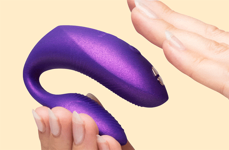 Hands holding purple We-Vibe Chorus Pro Haptic Remote for app-controlled couples vibrator on a white background.