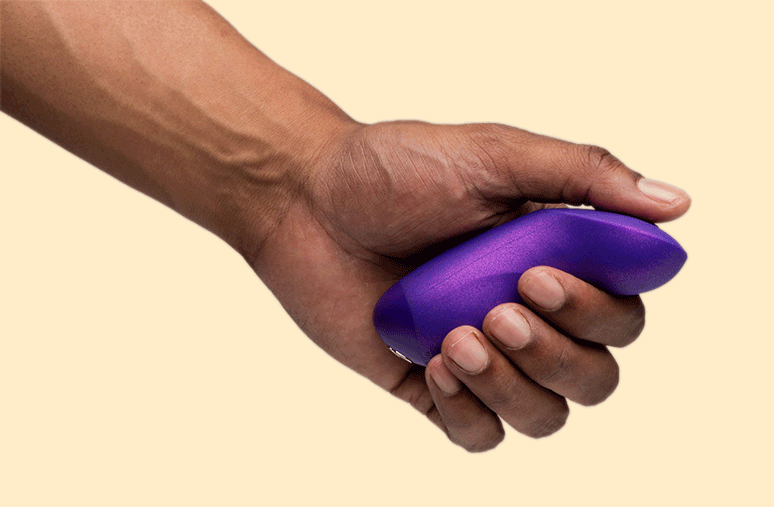 Hand holding purple We-Vibe Chorus Pro Haptic Remote for app-controlled couples vibrator on a white background.
